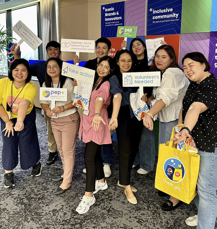 Employees holding PepsiCo Positive signs at an office event